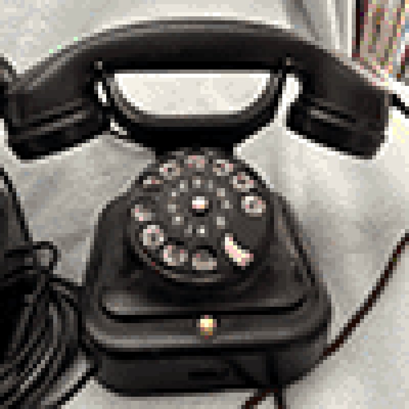 A vintage black rotary telephone with a circular dial featuring numbers 0-9 and letters A-K arranged in a circle. The image has been pixelated to a 100 x 100 grid and reduced to 256 colors, giving it a digitized appearance while still clearly showing the phone's classic design with handset resting on top of the base unit. The telephone sits on a light-colored surface with its cord visible.
