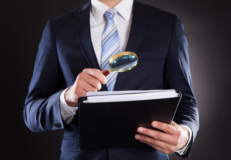 A professional in business attire holding a folder and magnifying glass, representing a manager or executive ready to conduct a Knowledge Gemba Walk to observe and analyze organizational knowledge flows.