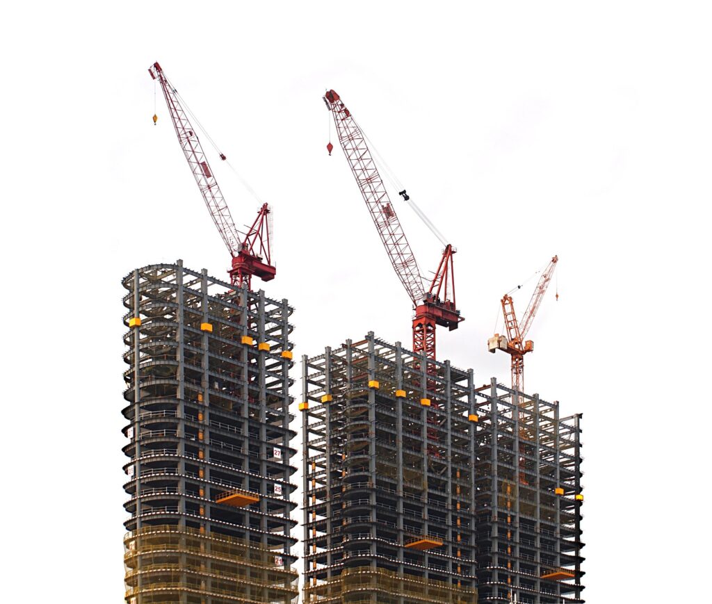 Steel frame construction of multiple skyscrapers under construction with red cranes against a bright sky. The exposed steel skeletons show the complex networking and hierarchical structure of load-bearing elements that normally remain invisible but enable the entire architecture. The image serves as a metaphor for metadata as epistemic infrastructure in organizations – like these steel beams, metadata forms the invisible yet fundamental structure that makes organizational intelligence and knowledge architectures possible.