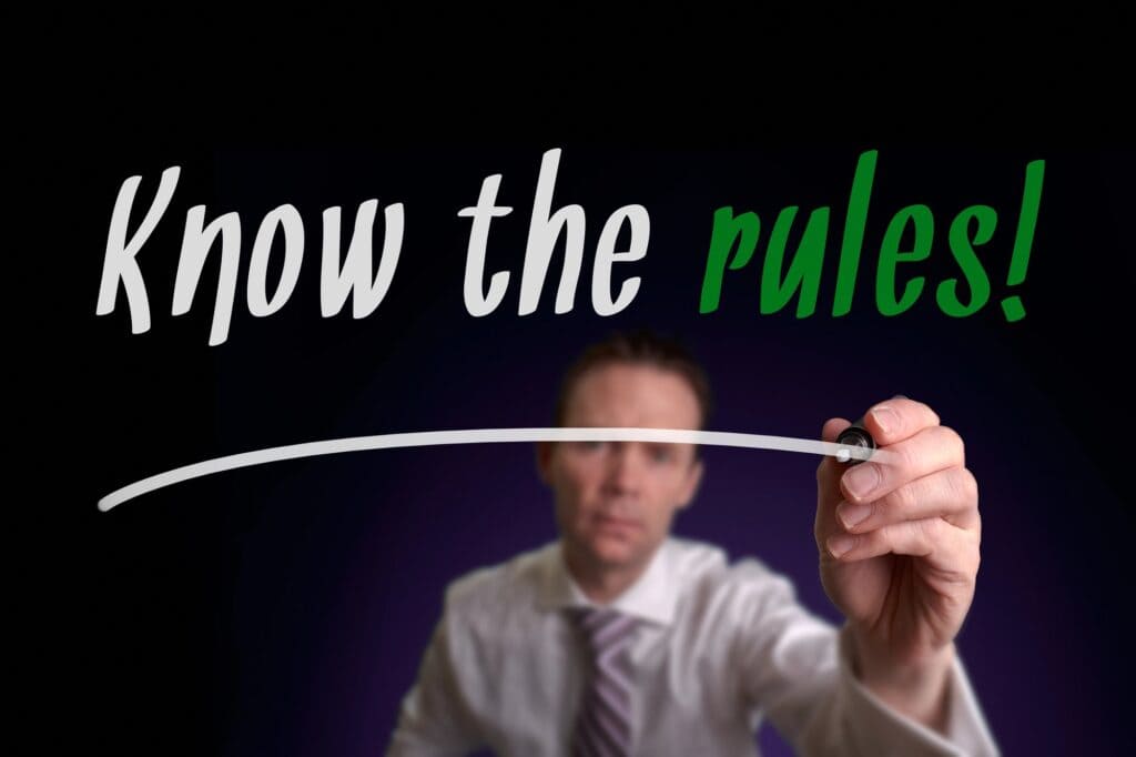 A businessman writing 'Know the rules!' on a transparent board, emphasizing the importance of guidelines in knowledge management.